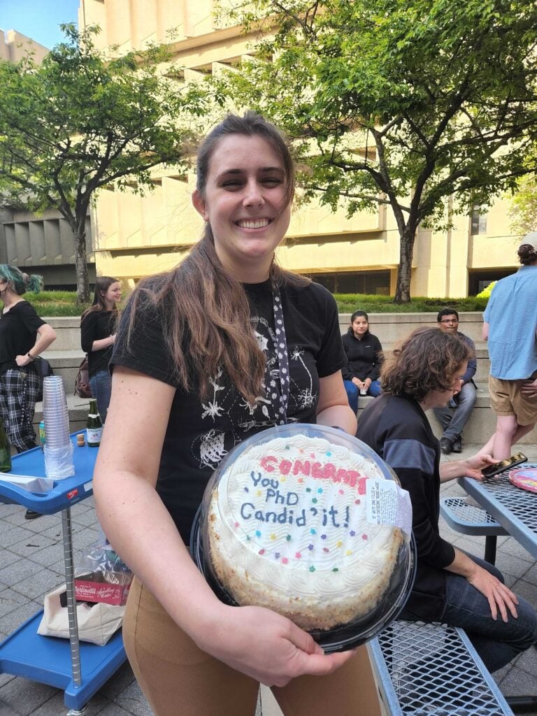 Lauren with her cake that says "Congrats, you PhD candid'it!"